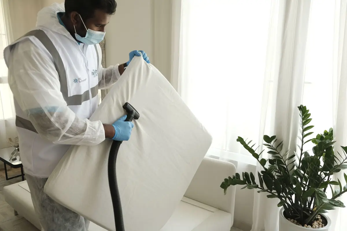 Technicien en combinaison qui traite un matelas à l’aspirateur